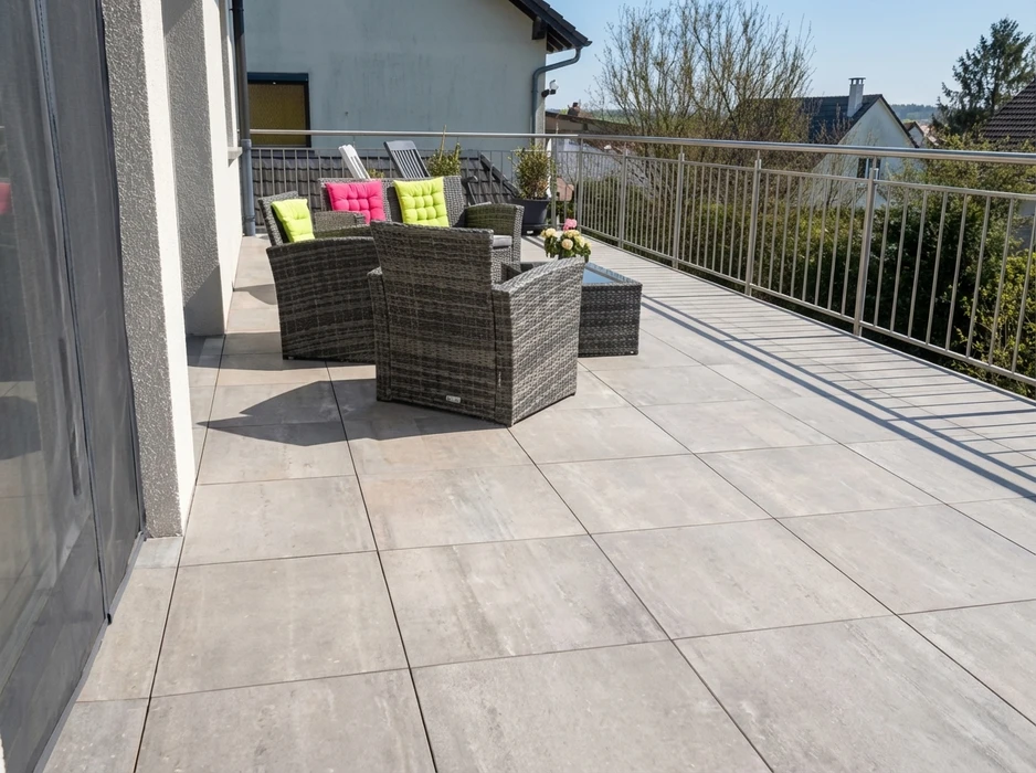 Terrasse extérieure en hauteur avec garde-corps métallique, mobilier de jardin en résine tressée gris avec coussins rose et vert anis, table basse vitrée