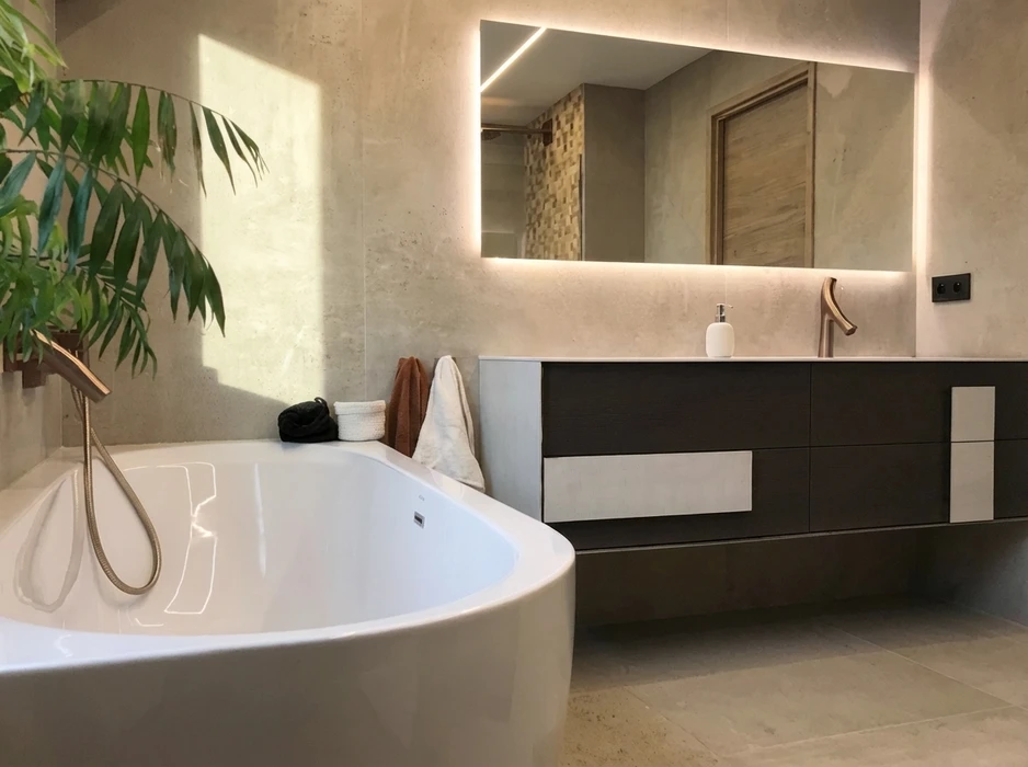 Salle de bain moderne et luxueuse avec baignoire îlot blanche autoportante, robinetterie dorée brossé, vasque à poser intégrée sur meuble suspendu bimatière bois foncé et façades laquées blanc