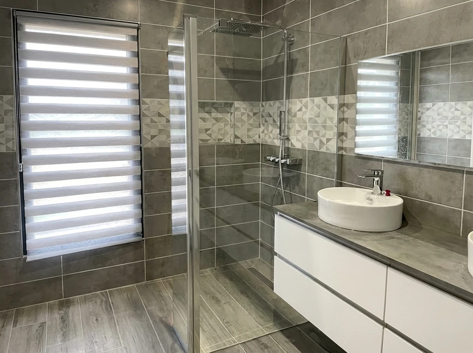 Salle de bain moderne avec douche à l'italienne en verre trempé, vasque à poser ronde en céramique blanche sur meuble suspendu laqué blanc avec plan en stratifié effet béton
