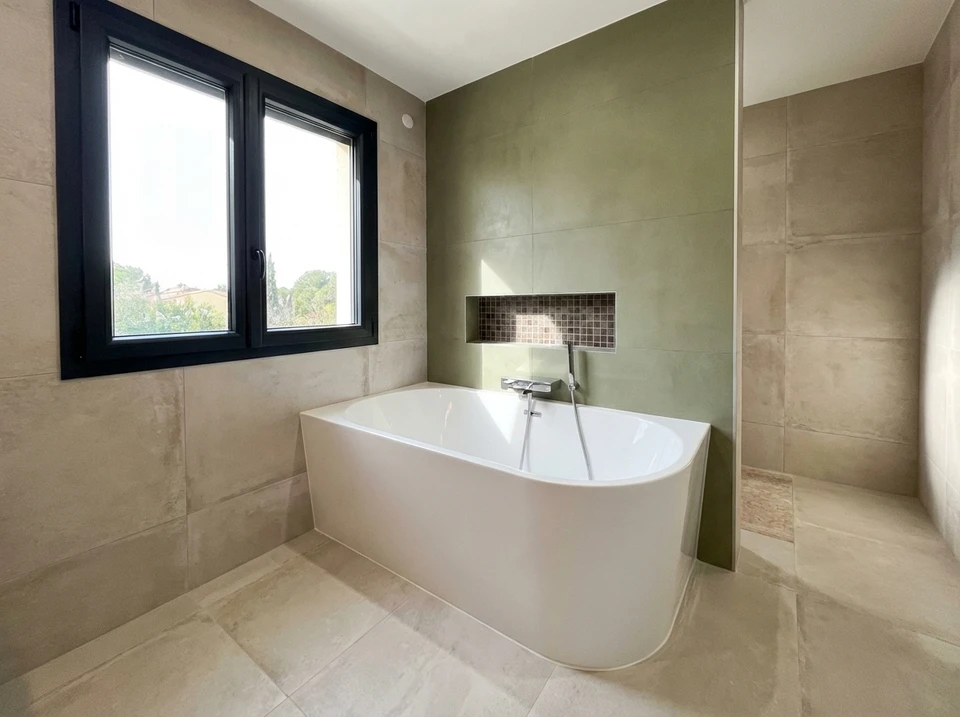 Intérieur de salle de bain en rénovation avec ouvrier appliquant du joint sur carrelage mosaïque
