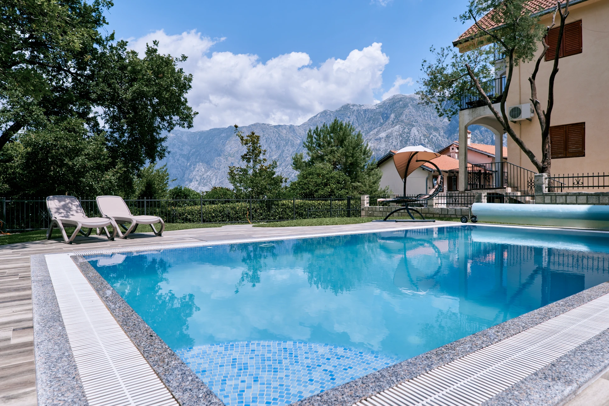 Terrasse extérieure moderne avec piscine rectangulaire à débordement, salon de jardin en rotin tressé marron avec coussins beiges disposé sous pergola bioclimatique à lames orientables blanches